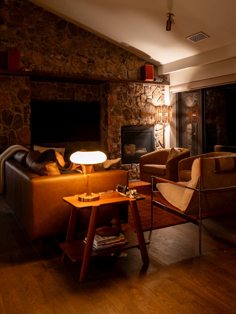 Warmly lit cabin living room with a stone fireplace and armchairs.
